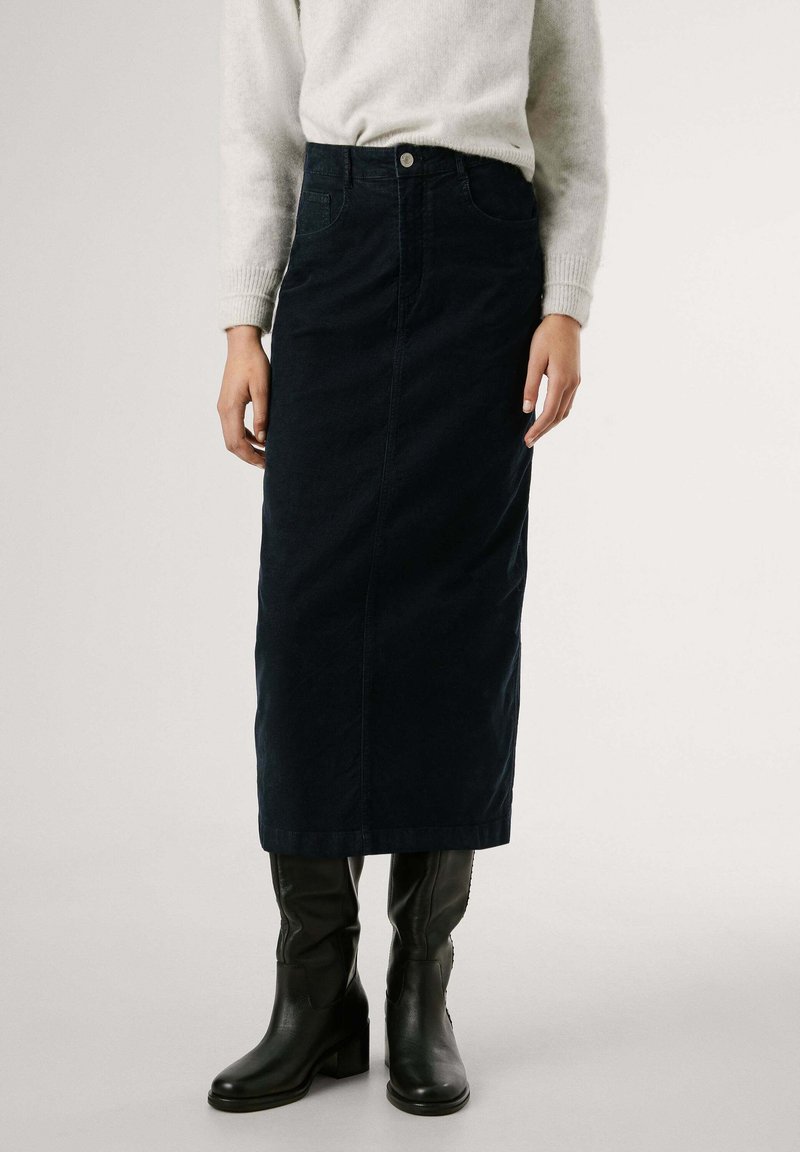 Dunkelblaue Denim-Midirock mit geradem Schnitt, Detailtaschen vorne und Knopfverschluss, kombiniert mit knielangen schwarzen Lederstiefeln.