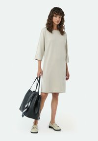 Hellgraues Kleid mit Dreiviertelärmeln, gerader Schnitt. Schwarze Handtasche mit einem gemusterten Schal, beige Slipper mit niedrigem Absatz.