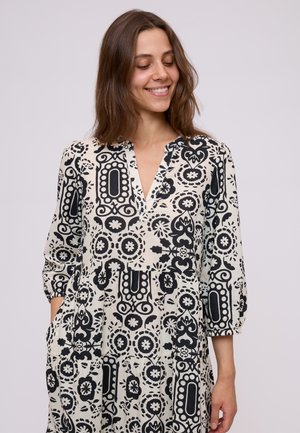 Rochie cu imprimeu alb-negru, cu decolteu adânc în V, mâneci trei sferturi și buzunare; prezintă designuri florale și geometrice.