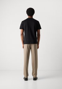 Tricou negru cu mânecă scurtă și guler rotund, asortat cu pantaloni bej și pantofi negri, prezentat din spate pe un fundal simplu.