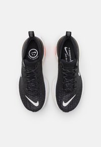 Le scarpe sportive nere presentano una tomaia in rete testurizzata, un sistema di allacciatura prominente e una suola intermedia bianca con accenti rossi sulla suola esterna.
