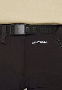 Svarta byxor med en W windwall-logotyp, tillsammans med ett svart bälte med texten "THE NORTH". Slät tyg med dragkedjedetalj på sidan.