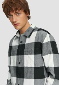 Zwart-witte geblokte shirt van zacht materiaal, met een kraag, knoopsluiting aan de voorkant en een borstzak.