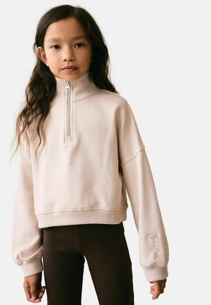 Felpa zip con colletto alto di colore rosa chiaro, spalle scese e polsini a coste. Abbinata a leggings marroni scuri. Dettaglio logo discreto.