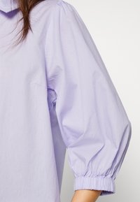 Lavandulová blůza s límečkem a nabíranými rukávy. Rukávy mají na manžetách nařasenou gumu pro lepší strukturu.