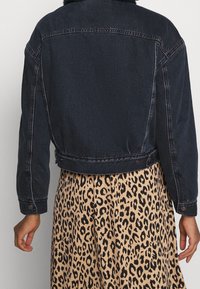 Mörk denimjacka med en figursydd design, med en pälskrage och knappade manschetter, bärs över en leopardmönstrad kjol med en flödande struktur.