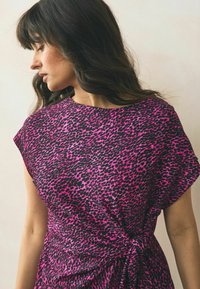Kortärmad klänning i stark rosa med svart leopardmönster, med en knuten midjedetalj och en avslappnad passform.