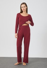 Burgundy fritidsklädeset med en långärmad topp med rundad halsringning och byxor med elastisk midja, båda med volangkanter och texturerad tyg.