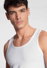Débardeur blanc à encolure ronde et bretelles fines, fabriqué en tissu lisse, ajusté au corps avec des coutures et des détails minimaux.