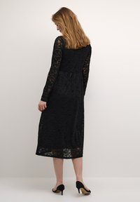 Svart spetsklänning med långa ärmar, knälång längd, blommönster, genomskinlig textur och en figurnära midja. Bärs med svarta klackskor.