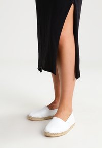 Vita canvas espadriller med en vävd jutesula, med en minimalistisk design och en slip-on stil, i kombination med ett svart plagg.