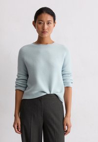 Jasnoniebieski sweter dzianinowy z okrągłym dekoltem i długimi rękawami, w połączeniu z ciemnymi spodniami w prążki. Miękka tekstura, luźny krój.