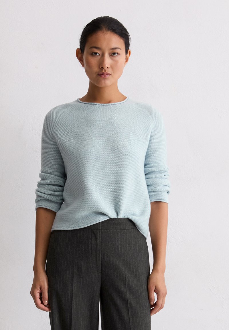 Jasnoniebieski sweter dzianinowy z okrągłym dekoltem i długimi rękawami, w połączeniu z ciemnymi spodniami w prążki. Miękka tekstura, luźny krój.