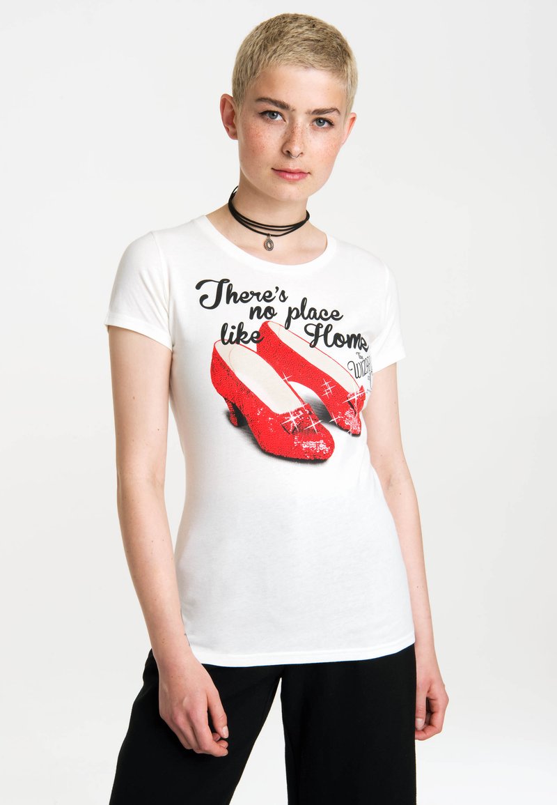 White t-shirt featuring a graphic of red sequined shoes, with text reading "There's no place like Home." Short sleeves and casual fit.