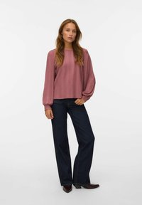 Chemisier rose à manches longues et texturé avec une coupe décontractée, associé à un jean taille haute bleu foncé à jambes larges et des chaussures à bout pointu.