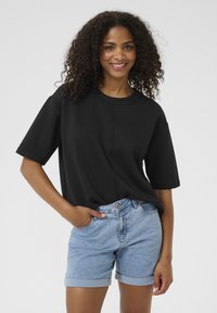 Black oversized short-sleeve t-shirt with a round neck, paired with light blue denim shorts featuring rolled hems and front pockets.