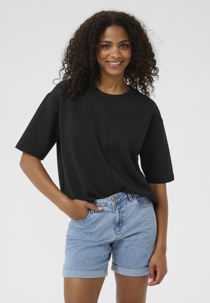 Black oversized short-sleeve t-shirt with a round neck, paired with light blue denim shorts featuring rolled hems and front pockets.