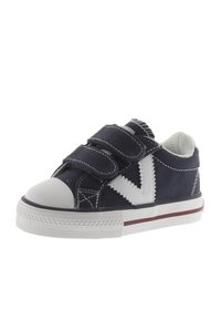 Scarpa di tela blu navy con accenti bianchi, punta tonda, cinturini in velcro e suola in gomma con una striscia rossa. Presenta dettagli di cuciture testurizzate.