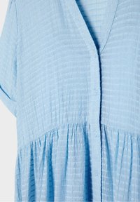 Robe en tissu texturé bleu clair avec manches courtes, boutonnée sur le devant et détail froncé à la taille.