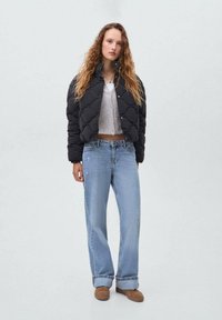 Veste matelassée noire avec un design court, associée �à un jean large bleu clair et un top court gris. Comprend des chaussures marron.