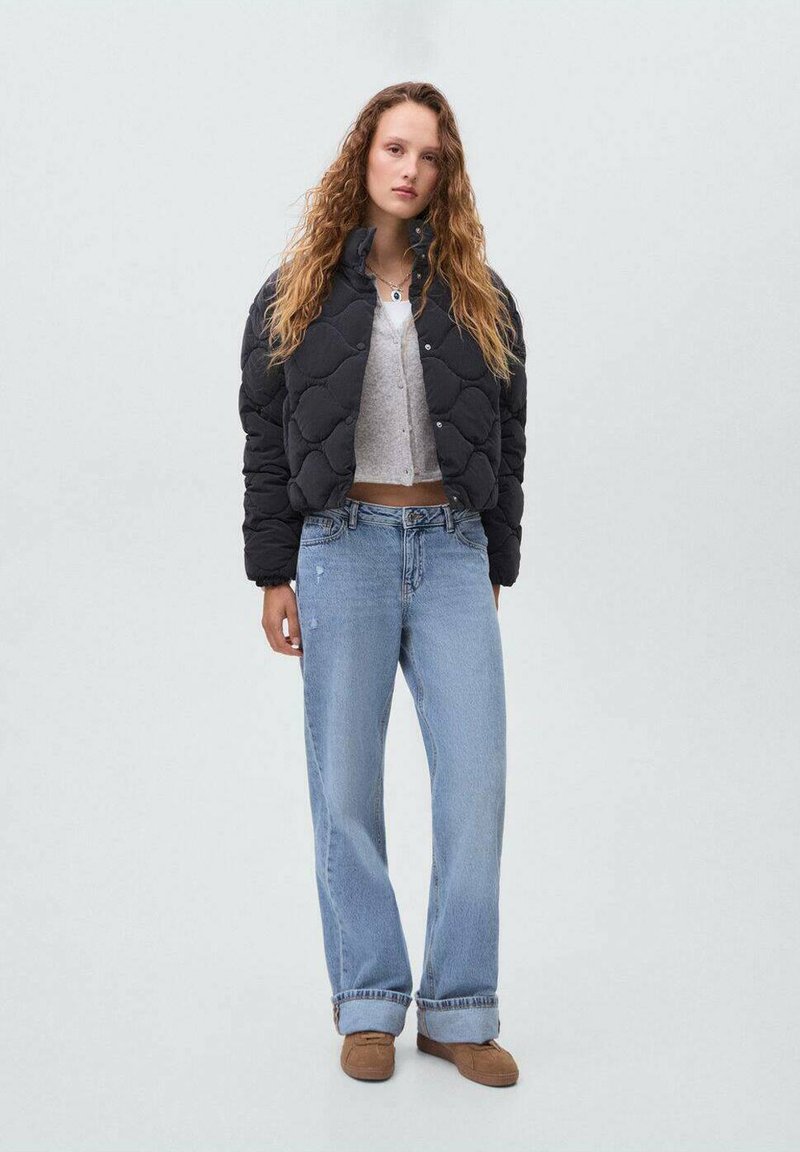 Veste matelassée noire avec un design court, associée à un jean large bleu clair et un top court gris. Comprend des chaussures marron.