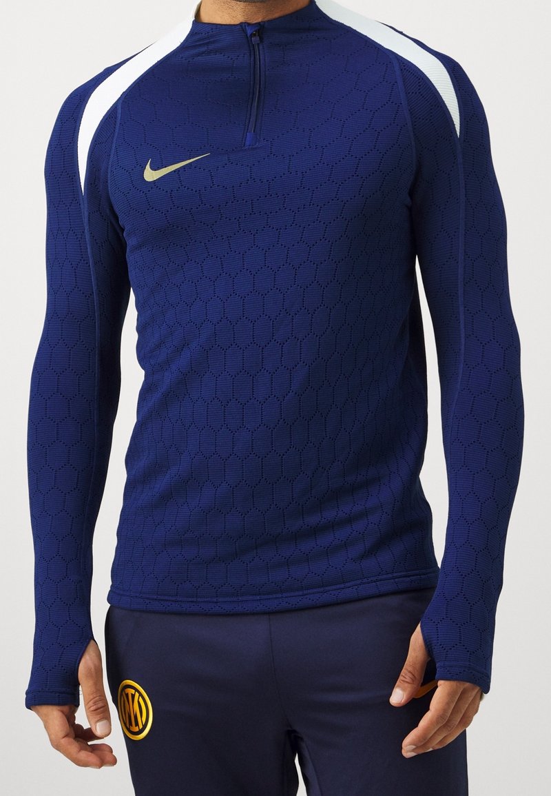 Navy long-sleeve athletic top with hexagonal texture, half-zip neck, and white shoulder accents. Features a gold Nike logo on the chest.