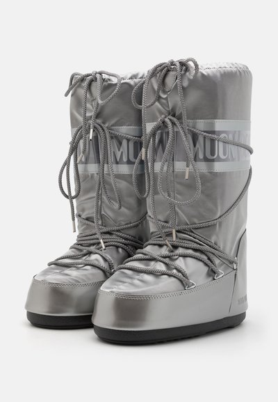 Bottes isolées grises avec une finition brillante, présentant des lacets, un col rembourré et une semelle texturée. Marque visible sur le côté.