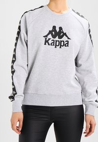 Felpa grigia in cotone con scollo rotondo, presenta il logo Kappa nero e strisce laterali a contrasto nere con loghi bianchi.