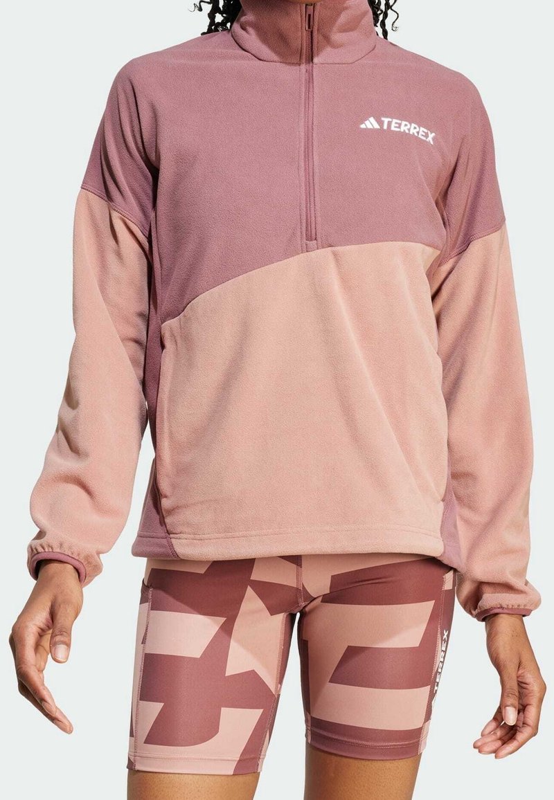 Pull polaire tons roses avec fermeture éclair à mi-hauteur, manches longues et col montant. Le short assorti à motifs complète la tenue.