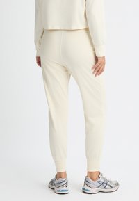 Crèmerfarvede bomuldsjoggers med en tapered pasform, der har ribbede manchetter og en glat tekstur, parret med grå og blå atletik sko.