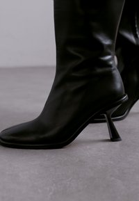 Svart läder ankelboot med spetsig tå och avsmalnande klack. Slät textur med en åtsittande passform, med en minimalistisk design och rena linjer.