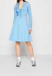 Sininen pitkähihaisen paita, jossa on pystysuorat raidat ja vetoketju, yhdistettynä vaaleansiniseen liehuvaan hameeseen. Mallilla on päällään hopeiset ja mustat lenkkarit.