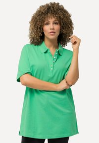 Zelená polo tričko s krátkým rukávem, vybavené knoflíkovou légu a volným střihem, vyrobené z měkkého materiálu s hladkou texturou.