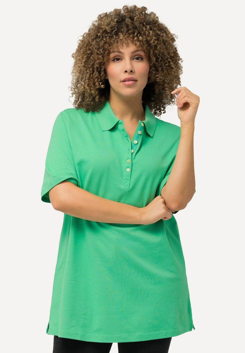 Zelená polo tričko s krátkým rukávem, vybavené knoflíkovou légu a volným střihem, vyrobené z měkkého materiálu s hladkou texturou.