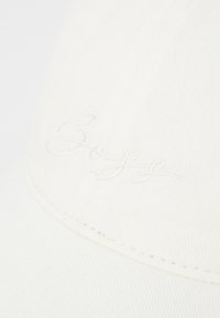 Weißer Baumwollhut mit gebogenem Schirm, genähten Nähten und gesticktem Branding in einer Schreibschrift auf der Vorderseite.