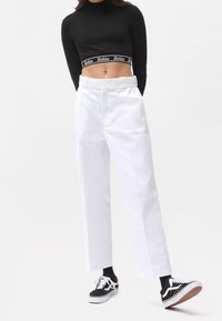 Valkoiset puuvillapantsit, jotka ovat löysät, korkealla vyötäröllä ja edessä taskuilla, yhdistetty mustaan lyhythihaiseen toppiin ja mustiin lenkkikengiin.