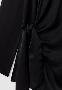 Tessuto nero con una consistenza liscia, caratterizzato da un accento annodato e un design drappeggiato, creando un aspetto fluido e stratificato.