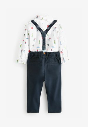 Bela srajca s kratkimi rokavi z izrazitimi barvnimi risanimi motivi in temno modre hlače z naramnicami, ki imajo pikčasto vzorec in gumb na hrbtni strani.