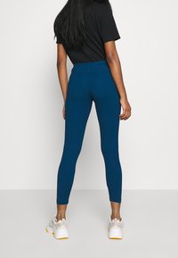 Högmidjade tights i teal, tillverkade av stretchigt material, med en slät yta och åtsittande design. Kombinerat med vita sportskor.