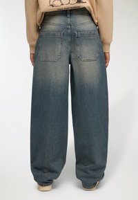 Jeans in denim a gamba larga in un lavaggio blu sbiadito, con due tasche posteriori e un vita alta. Il tessuto ha un aspetto morbido e strutturato.