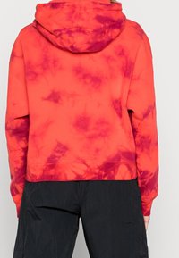 Rød tie-dye hoodie med lilla detaljer, har hætte, sænkede skuldre og en cropped pasform. Lavet af blødt stof med en struktureret finish.