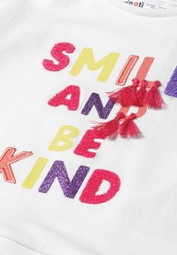 Weißes Baumwoll-T-Shirt mit mehrfarbiger, strukturierter Stickerei des Satzes "Lächeln und freundlich sein" und pinken Quasten an zwei Buchstaben.