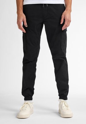 Black cargo pants made of cotton blend, featuring multiple side pockets, elastic cuffs, and a relaxed fit. Paired with white sneakers.