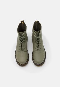 Bottines en cuir vert avec un bout arrondi et un laçage. Comprend des coutures jaunes et une tirette en boucle au talon pour un enfilage facile.
