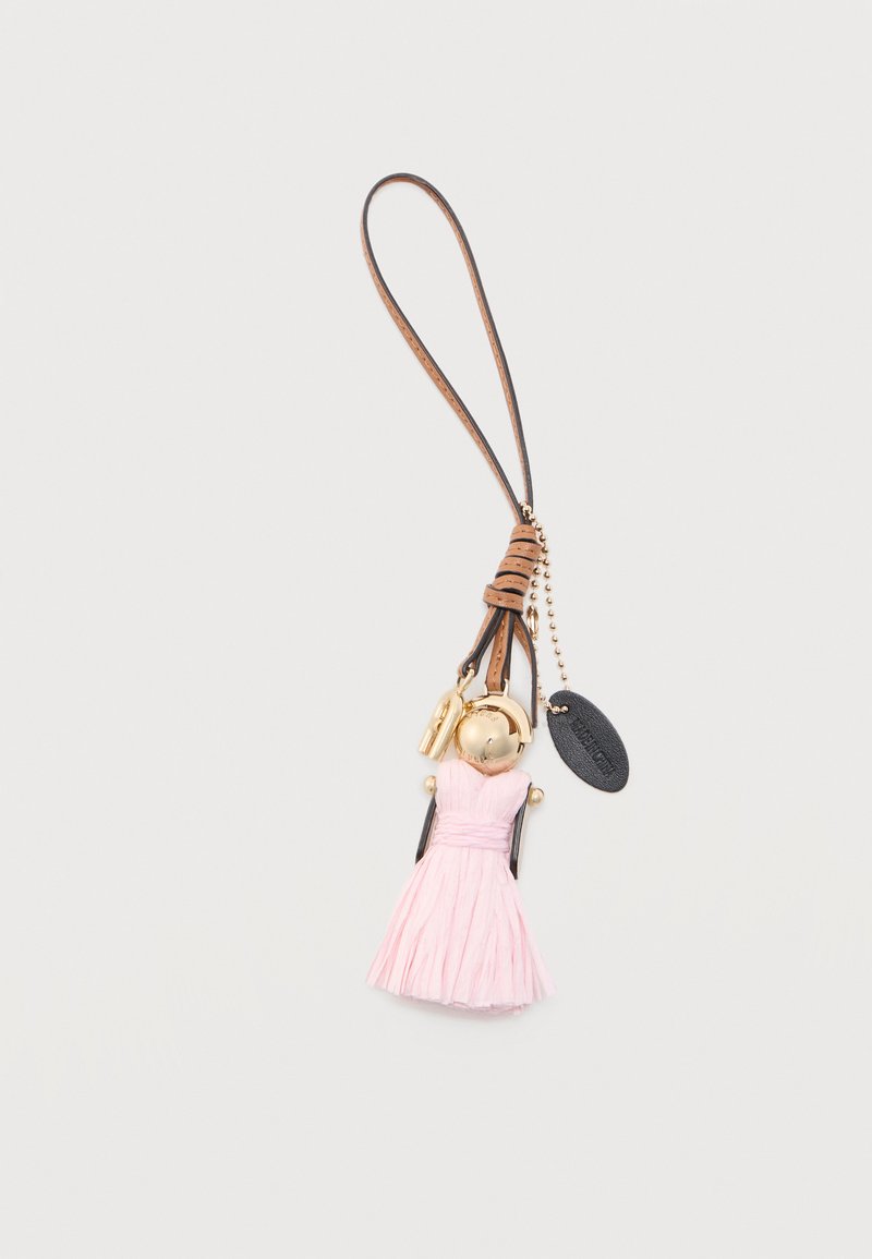 Μπρελόκ σε σχήμα κούκλας με ροζ φόρεμα, χρυσή κεφαλή και καφέ λουράκι από δέρμα, προσαρτημένο σε χρυσή αλυσίδα και μαύρη ετικέτα.