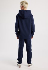 Sweat à capuche bleu marine et pantalon de jogging assorti, fabriqués en tissu doux. Présente des poignets et un ourlet côtelés, ainsi que des baskets à carreaux faciles à enfiler.