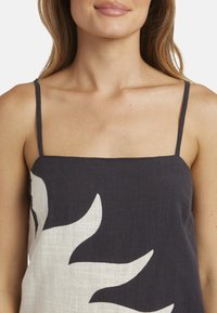 Vrouw in een zwart-witte mouwloze jurk met dunne bandjes en een groot abstract patroon aan de voorkant.