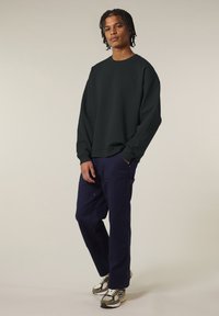 Felpa verde scuro con polsini e orlo a coste, abbinata a pantaloni cargo blu navy con multiple tasche e hardware argentato.