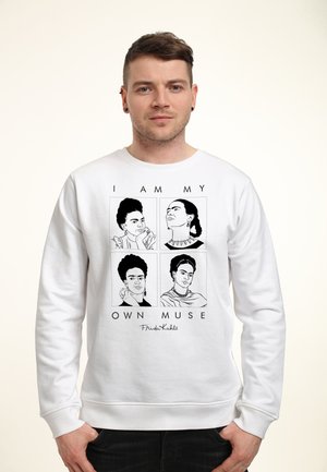 Mand iført hvid sweatshirt med fire sort-hvide skitser af Frida Kahlo og teksten "I am my own muse" foran.