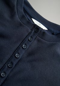 Marineblauwe geribbelde gebreide stof met een ronde hals en een knoopsluiting met zes zwarte knopen, textuur voor comfort.